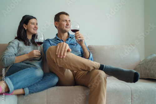 Young romantic couple sitting on sofa at home drinking red wine. © Space_Cat