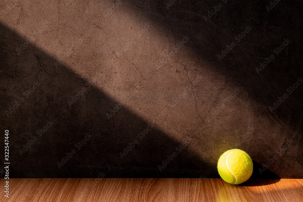 Tennis ball on a wooden table with light and shadow on old gray concrete walls.