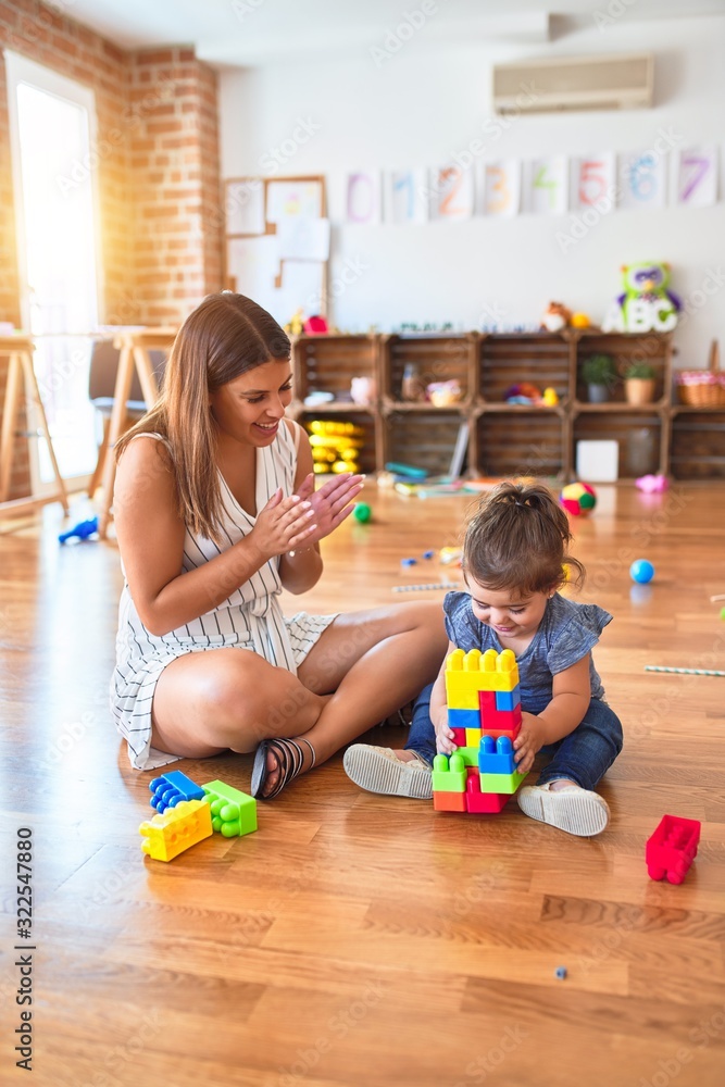 Fototapeta premium Young beautiful teacher and toddler playing with building blocks toy at kindergarten