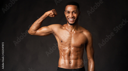 Smiling black man showing body on dark gray wall © Prostock-studio