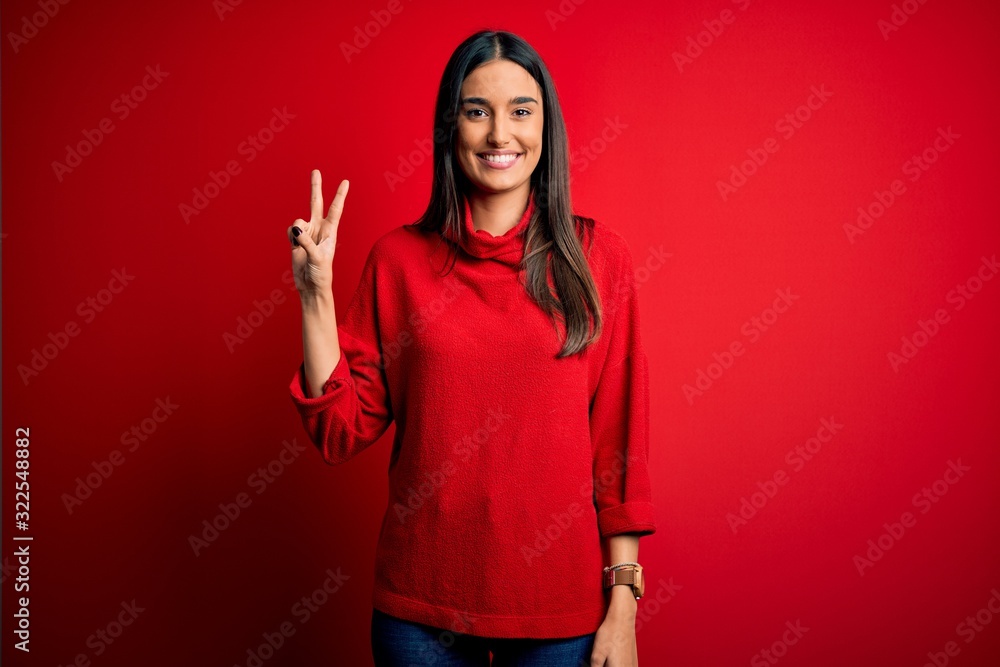 Young beautiful brunette woman wearing casual sweater over isolated red background showing and pointing up with fingers number two while smiling confident and happy. Young beautiful brunette woman wearing casual sweater over isolated red background showing and pointing up with fingers number two while smiling confident and happy.