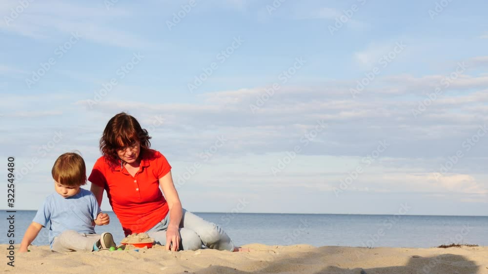 Mother playing with little child boy on sand beach. Adult woman and her son enjoying summer day on seshore. Family holiday at sea. Slow motion Mother playing with little child boy on sand beach. Adult woman and her son enjoying summer day on seshore. Family holiday at sea. Slow motion