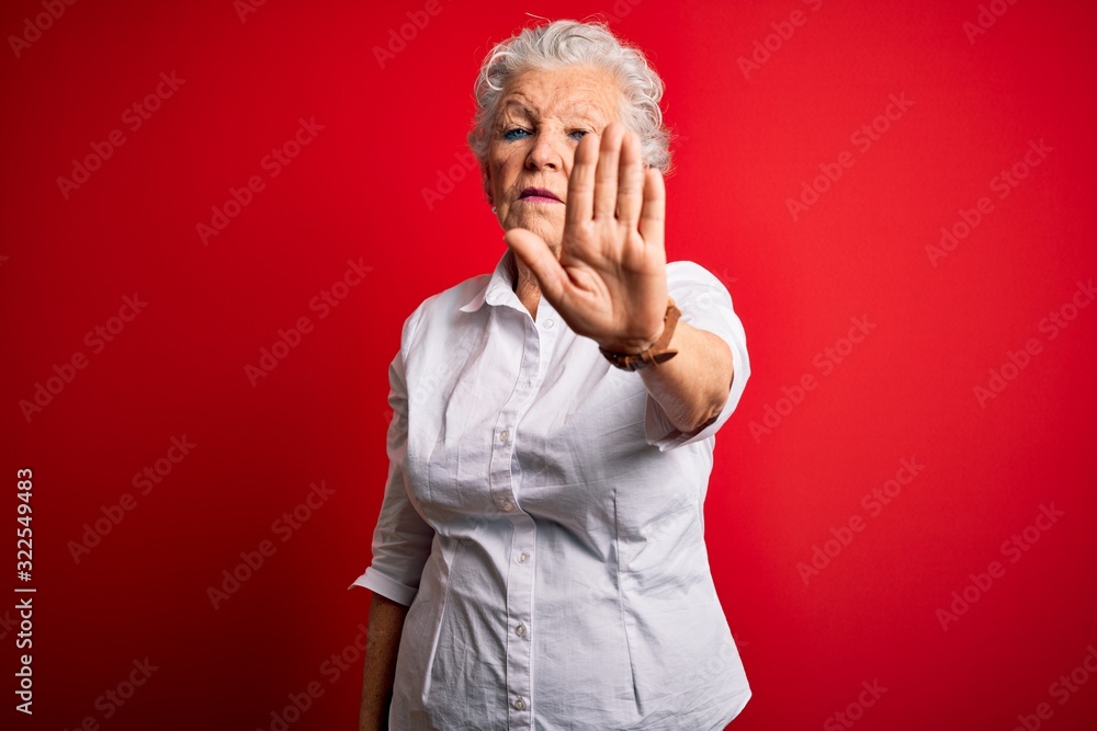 Senior beautiful woman wearing elegant shirt standing over isolated red background doing stop sing with palm of the hand. Warning expression with negative and serious gesture on the face.