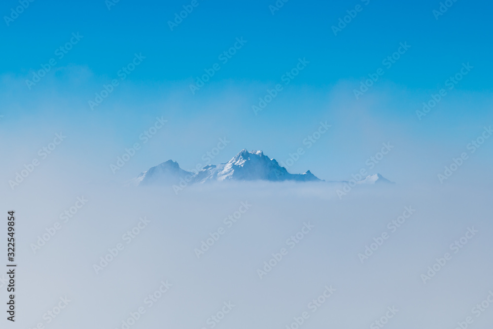 Fototapeta premium summit of Pilatus mountain sticking out of sea of fog with blue sky