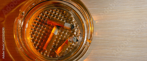 Glass ashtray with three cigarette butts on wood background copy space