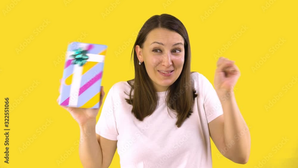 Young Woman in White T-shirt Holds Beautiful Box with a Gift and Rejoices. Back Yellow Background. Holiday Mood. Young Woman in White T-shirt Holds Beautiful Box with a Gift and Rejoices. Back Yellow Background. Holiday Mood.