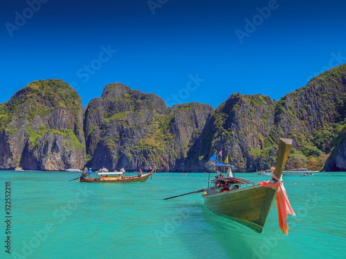 view of long-tail boats floating and running in blue-green sea with rock mountains and blue sky background, Ao Loh Samah Bay, Mu Ko Phi Phi islands, Krabi, southern of Thailand. © Yuttana Joe