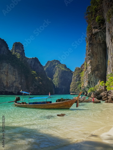view of a long-tail boat floating in blue-green sea around with high rock mountains and blue sky background, Ao Loh Samah, Mu Ko Phi Phi islands, Krabi, southern of Thailand.