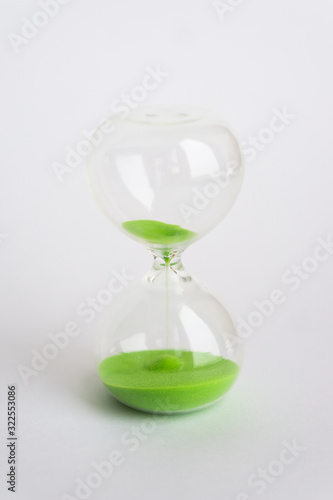 Hourglass with green sand on white background.