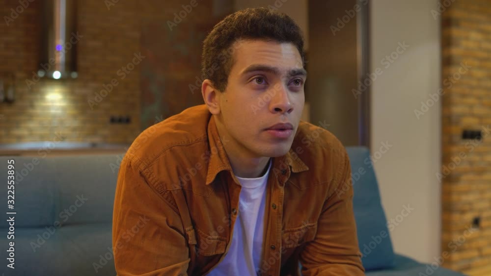 Excitement emotions on face of mixed-race guy watching tv show on couch at home Excitement emotions on face of mixed-race guy watching tv show on couch at home