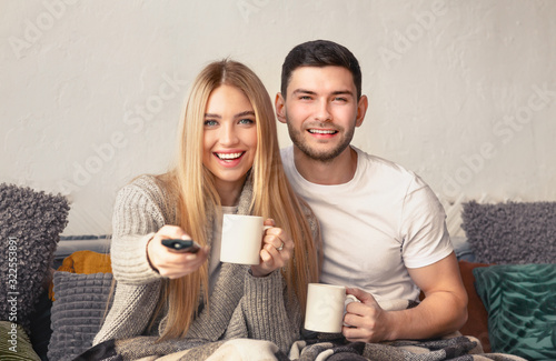 Cheerful millennial couple drinking tea and watching TV