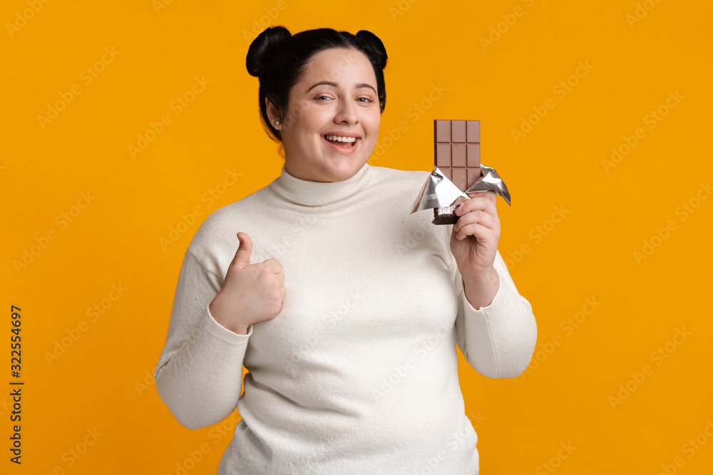 Joyful Overweight Girl Holding Chocolate Bar And Showing Thumb Up Joyful Overweight Girl Holding Chocolate Bar And Showing Thumb Up