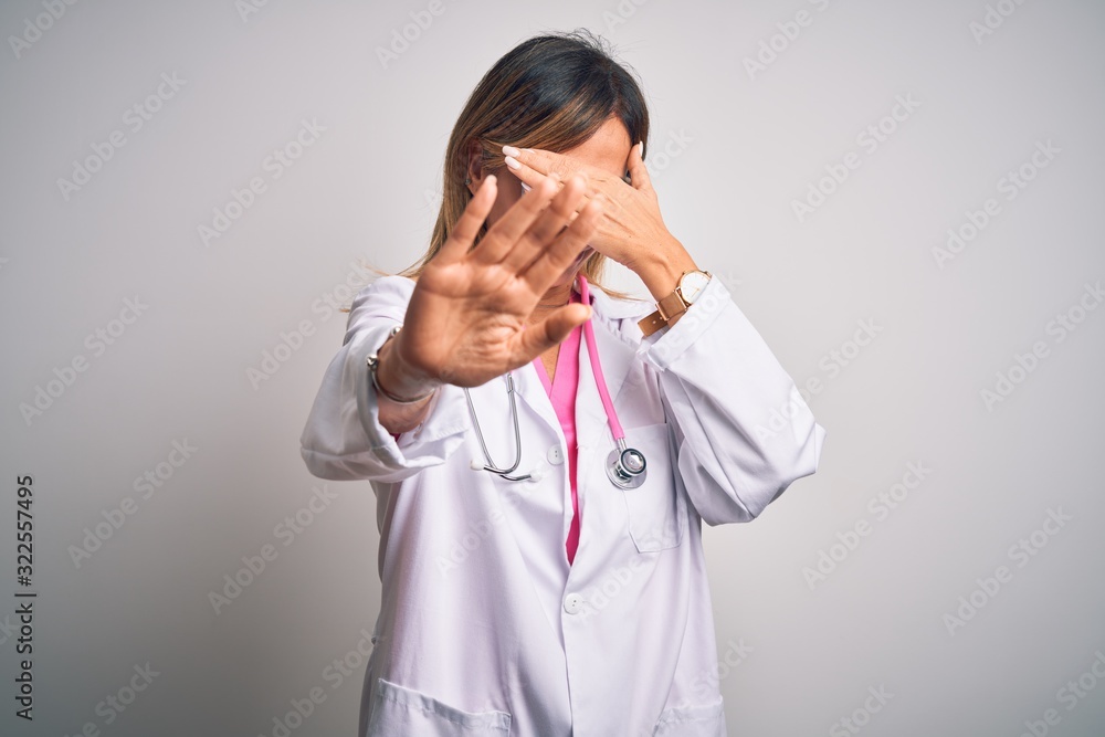 Middle age beautiful doctor woman wearing pink stethoscope over isolated white background covering eyes with hands and doing stop gesture with sad and fear expression. Embarrassed and negative concept Middle age beautiful doctor woman wearing pink stethoscope over isolated white background covering eyes with hands and doing stop gesture with sad and fear expression. Embarrassed and negative concept