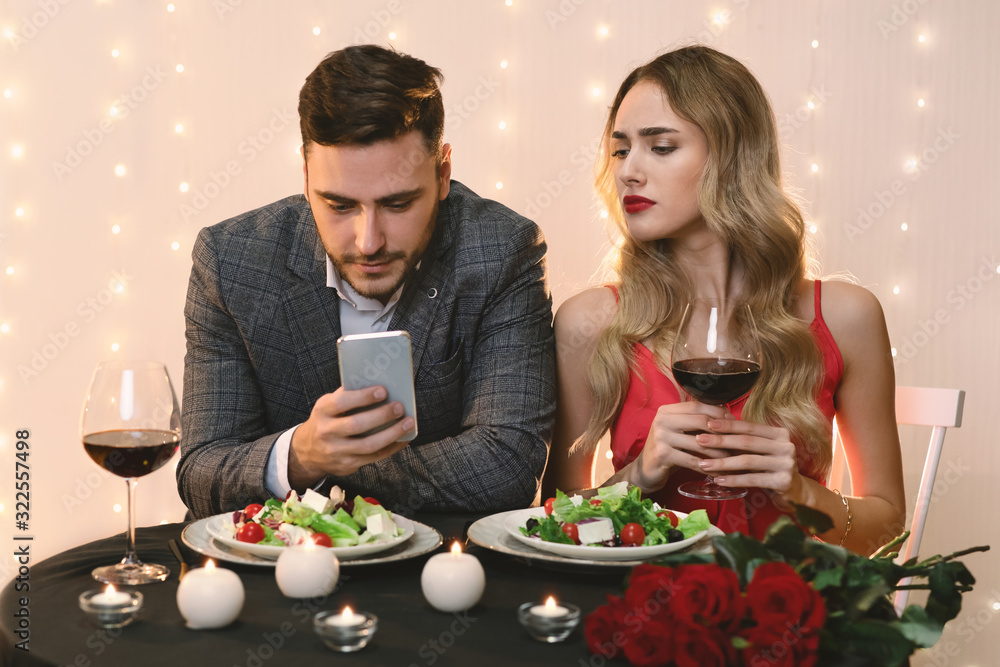 Jealous Woman Pekking Into Boyfriend's Smartphone During Dinner In Restaurant Jealous Woman Pekking Into Boyfriend's Smartphone During Dinner In Restaurant