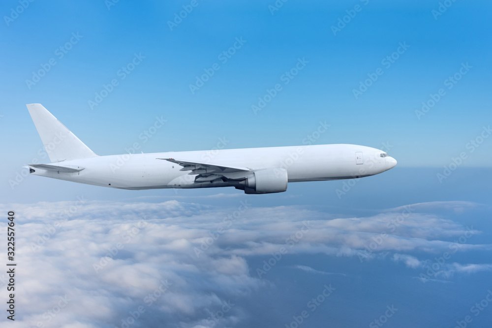 Fototapeta Cargo plane without portholes flying in the sky above the clouds.