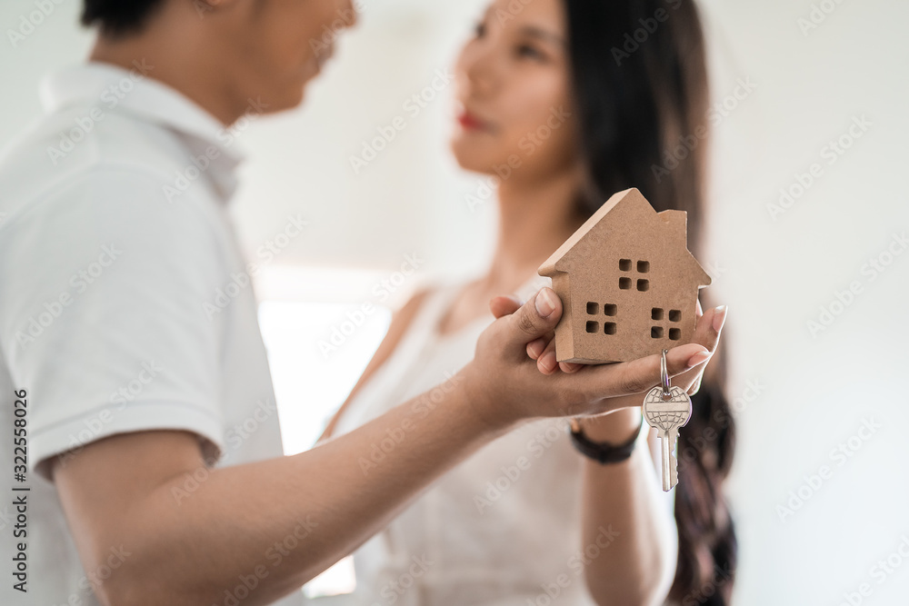 Happy smiling asian couple holding a model house, and danceing together with feeling happiness. Young loving couple with small wooden house new home concept Happy smiling asian couple holding a model house, and danceing together with feeling happiness. Young loving couple with small wooden house new home concept