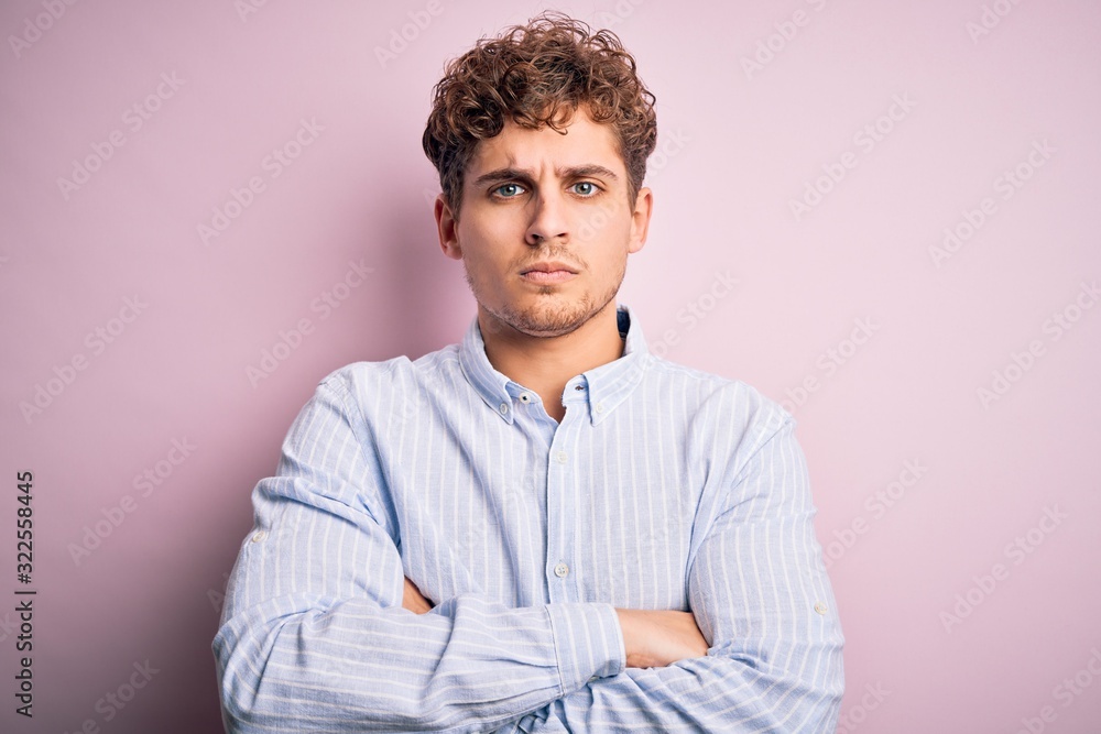 Young blond handsome man with curly hair wearing striped shirt over white background skeptic and nervous, disapproving expression on face with crossed arms. Negative person. Young blond handsome man with curly hair wearing striped shirt over white background skeptic and nervous, disapproving expression on face with crossed arms. Negative person.