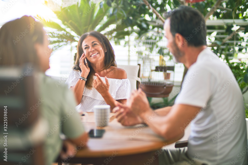 Beautiful family sitting on terrace drinking cup of coffee talking on the smartphone and smiling Beautiful family sitting on terrace drinking cup of coffee talking on the smartphone and smiling