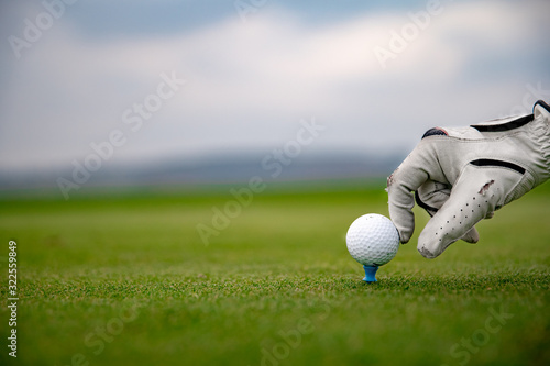 hand in white leather glove straightens golf ball on green golf course