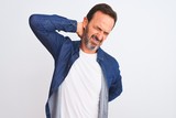 Middle age handsome man wearing blue denim shirt standing over isolated white background Suffering of neck ache injury, touching neck with hand, muscular pain