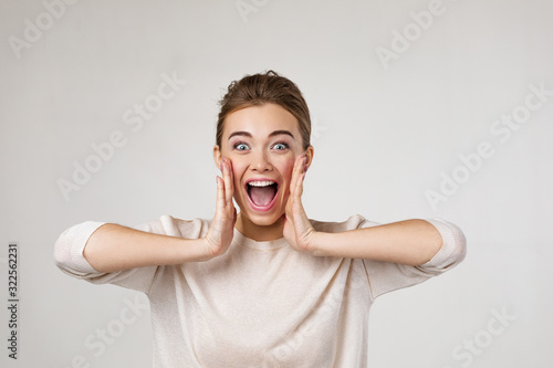 Portrait of young surprised beautiful woman screaming with shocked facial expression on gray background