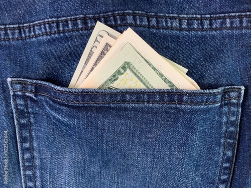 Dollars in the back pocket of men's jeans. Banknotes of American money in blue jeans. American currency peeps out of clothes.