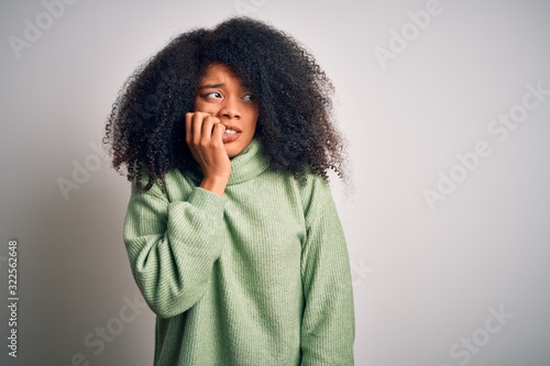 Young beautiful african american woman with afro hair wearing green winter sweater looking stressed and nervous with hands on mouth biting nails. Anxiety problem. © Krakenimages.com