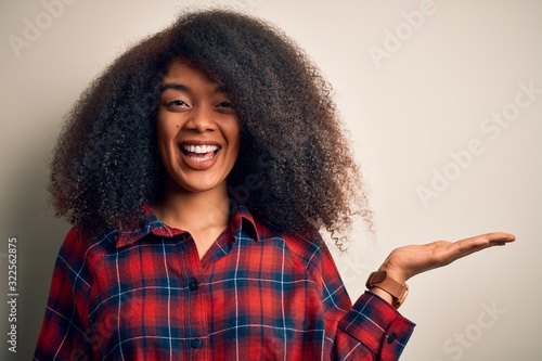 Young beautiful african american woman wearing casual shirt over isolated background smiling cheerful presenting and pointing with palm of hand looking at the camera. © Krakenimages.com
