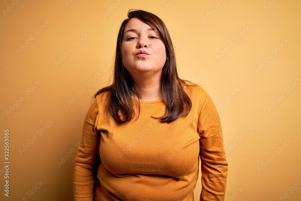 Obraz premium Beautiful brunette plus size woman wearing casual sweater over isolated yellow background looking at the camera blowing a kiss on air being lovely and sexy. Love expression.