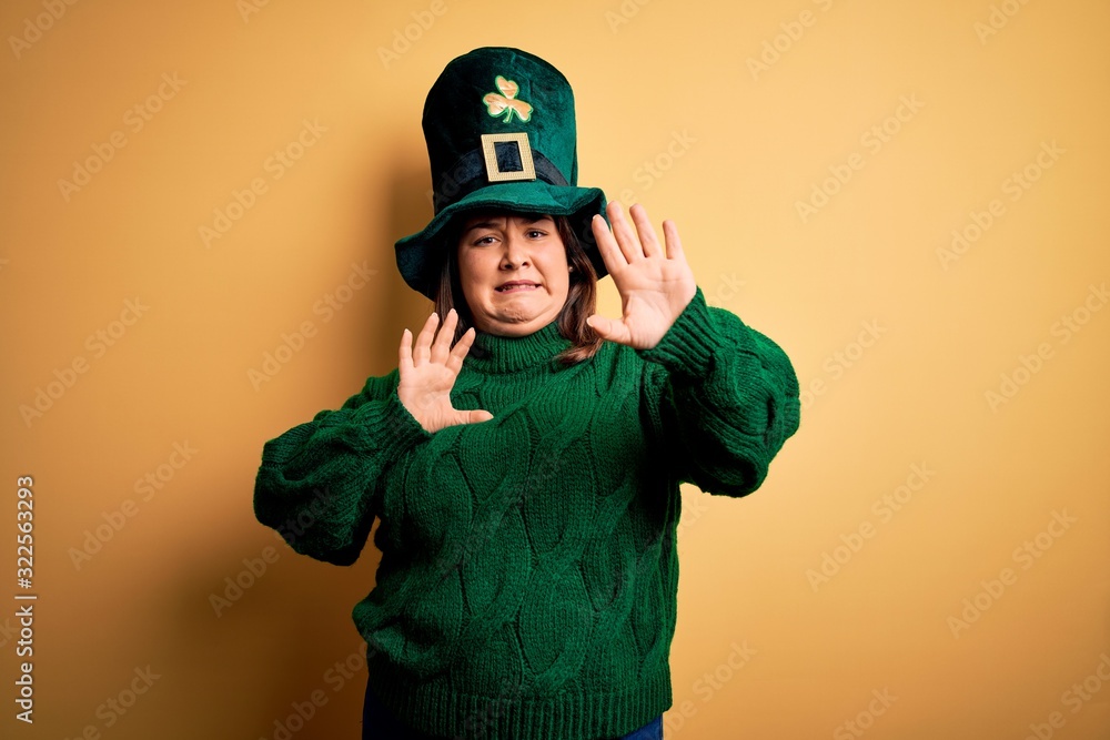 Young beautiful plus size woman wearing green hat with clover celebrating saint patricks day afraid and terrified with fear expression stop gesture with hands, shouting in shock. Panic concept. Young beautiful plus size woman wearing green hat with clover celebrating saint patricks day afraid and terrified with fear expression stop gesture with hands, shouting in shock. Panic concept.