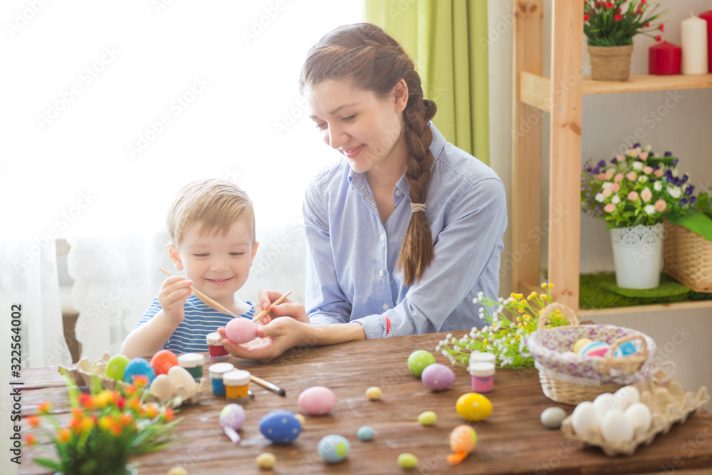 Mother and her son painting colorful easter eggs. Family celebrating Easter. Parent and kid play indoors. Decorated home and spring flowers Mother and her son painting colorful easter eggs. Family celebrating Easter. Parent and kid play indoors. Decorated home and spring flowers
