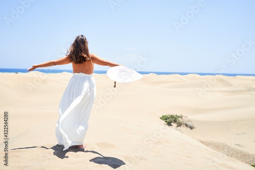 Young beautiful woman sunbathing with open arms enjoying summer vacation at maspalomas dunes beach photo