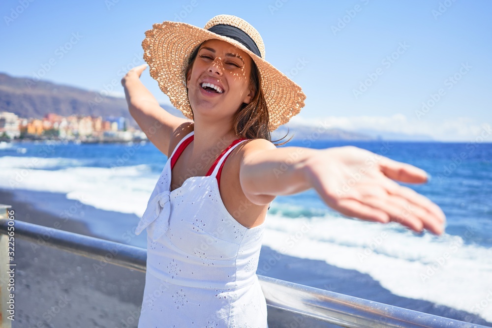 Young beautiful woman smiling happy, sunbathing with open arms enjoying summer vacation at the beach