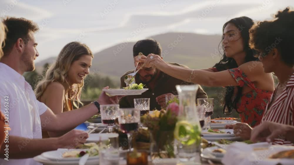 Woman serving food to friends having dinner at party table. Group of men and women having a dinner party outdoors. Woman serving food to friends having dinner at party table. Group of men and women having a dinner party outdoors.