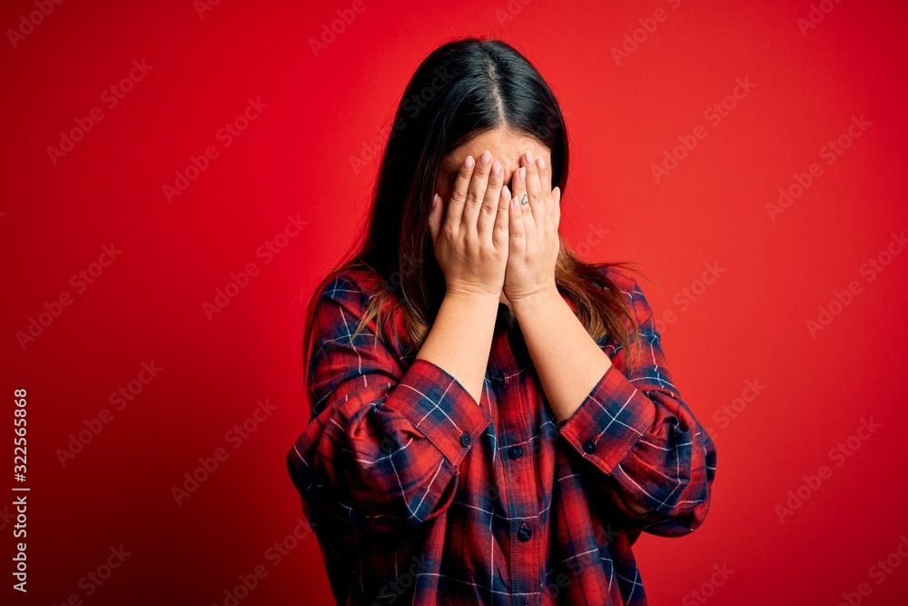 Young beautiful woman wearing casual shirt over red background with sad expression covering face with hands while crying. Depression concept. Young beautiful woman wearing casual shirt over red background with sad expression covering face with hands while crying. Depression concept.