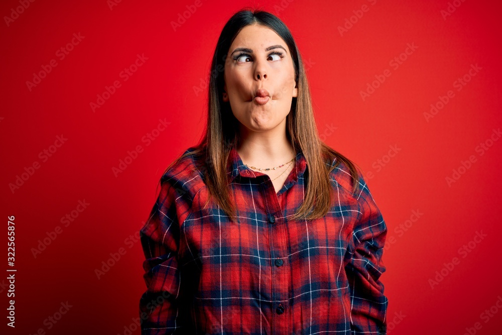 Young beautiful woman wearing casual shirt over red background making fish face with lips, crazy and comical gesture. Funny expression. Young beautiful woman wearing casual shirt over red background making fish face with lips, crazy and comical gesture. Funny expression.