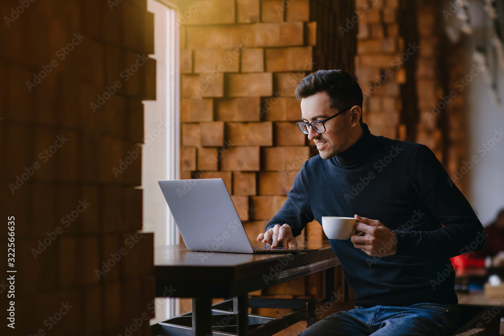 Happy smiling man working at laptop. Surprised smiling man holding a cup of coffee in his hand and looking at laptop. Happy smiling man working at laptop. Surprised smiling man holding a cup of coffee in his hand and looking at laptop.
