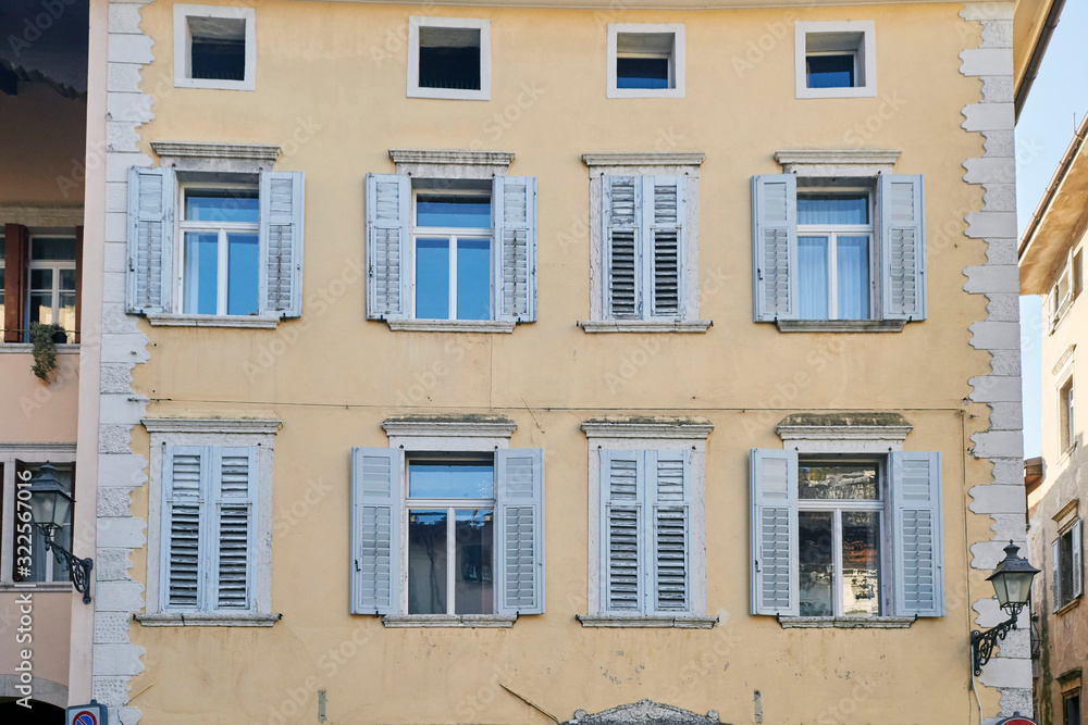 Eight italian windows on the yellow wall facade with wooden shabby white color shutters
