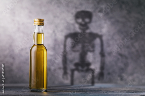 A bottle of whiskey with a shadow in the shape of a skeleton. Concept on the harm of alcohol and harmful habits of man