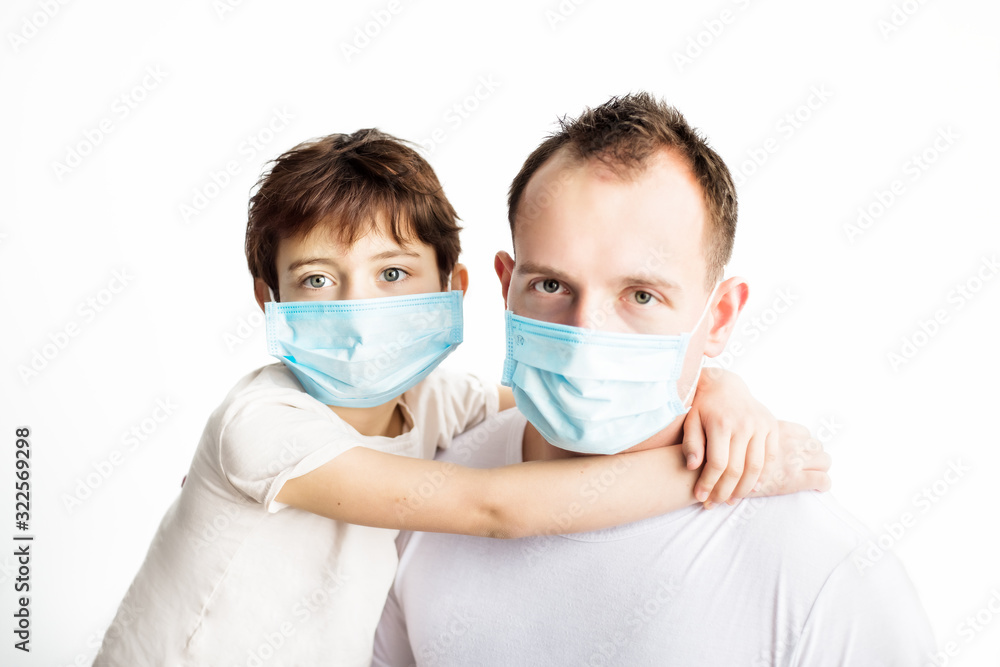 Child and dad in blue medical masks and white t-shirts hugging each other and looking in camera on white background. Coronavirus protection. Medical care. Illness covid-2019 prevention Child and dad in blue medical masks and white t-shirts hugging each other and looking in camera on white background. Coronavirus protection. Medical care. Illness covid-2019 prevention