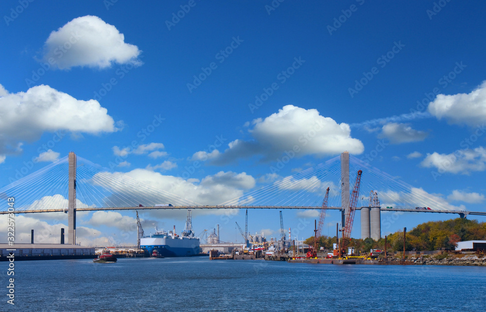 A busy harbor with freighters and tugboats beneath a suspension bridge