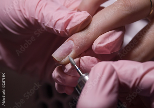 The manicurist cleans the cuticle of the nails with the device. Cuticle removal using a machine with a cutter. Professional manicure in the salon close-up.