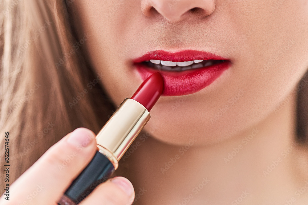 Woman applying bright matte red lipstick on her lips close up