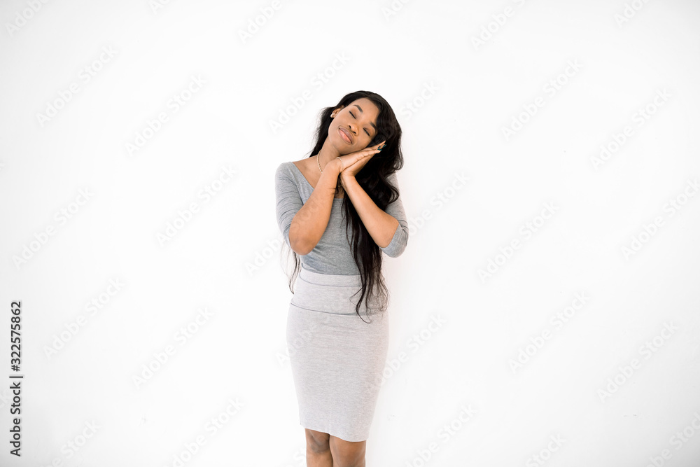 Tired african american woman in gray dress put head on folded hands, feeling sleepy, daydreaming. Pretty young african woman sleeping, relaxing isolated on white studio background. Tired african american woman in gray dress put head on folded hands, feeling sleepy, daydreaming. Pretty young african woman sleeping, relaxing isolated on white studio background.