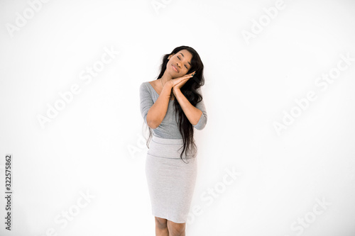 Tired african american woman in gray dress put head on folded hands, feeling sleepy, daydreaming. Pretty young african woman sleeping, relaxing isolated on white studio background.