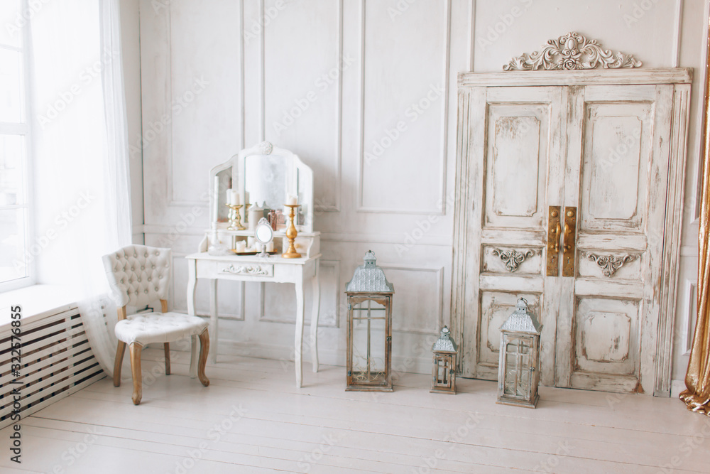 beautiful  light interior. classic room with wooden floor white walls with moldings, dressing  table with mirror decorated with elements, chair, sofa, lanterns, gold curtains vintage old door - obrazy, fototapety, plakaty 