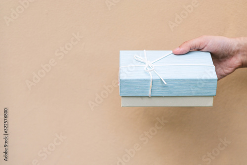 Close up of female hands holding a small blue gift box with white ribbon on yellow background.