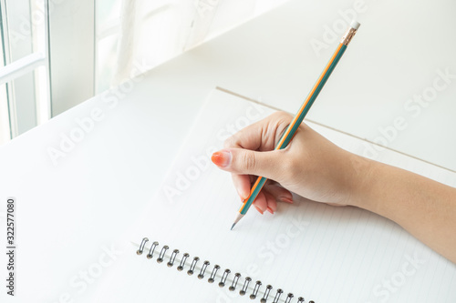 Close up female's hand writing on a notebook paper with pencil