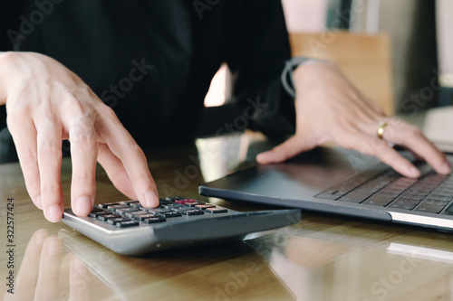 Close up Businesswoman using calculator and laptop for do math finance on wooden desk in office and business working background, tax, accounting, statistics and analytic research concept