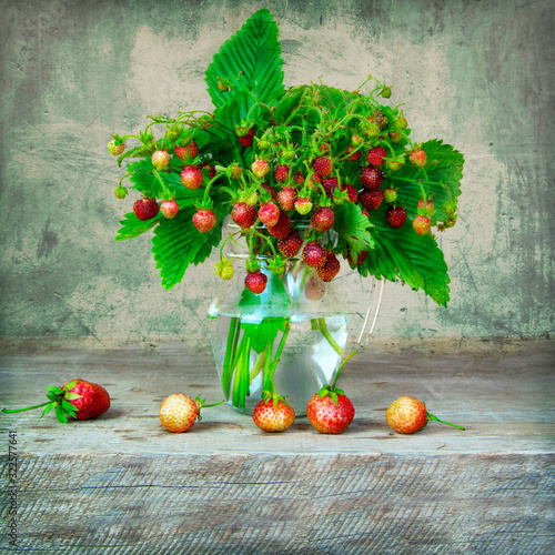 Still life with whild strawberries in glass vase on wooden table photo